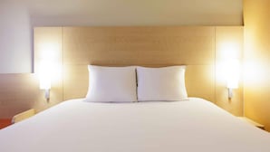 A neatly made bed with two pillows and two wall-mounted lamps on either side.