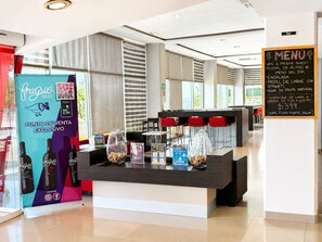 A hotel reception area with a counter, a menu board, and a promotional stand for a wine brand. - ibis Aguascalientes Norte (Aguascalientes)