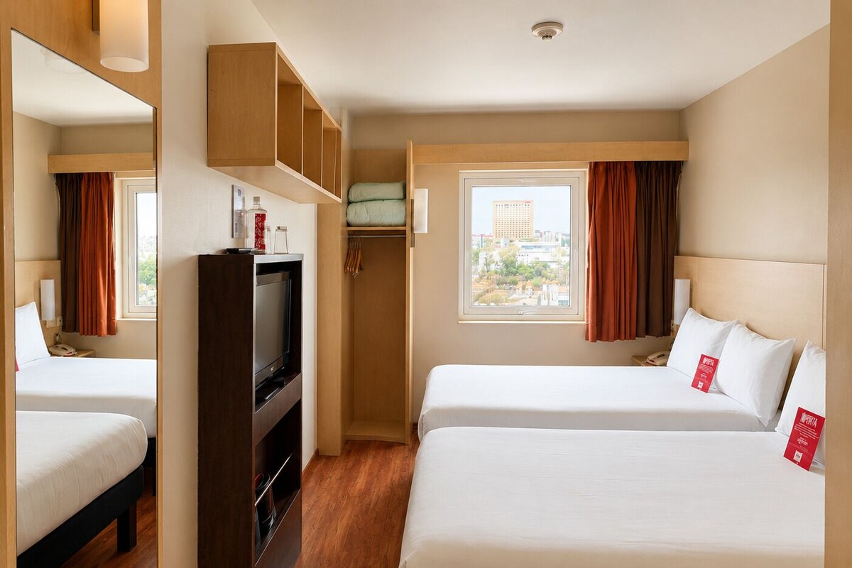 A hotel room with two beds, a TV, a wardrobe, and a window with curtains.