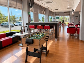 A modern indoor space with a foosball table, red seating, and large windows.
