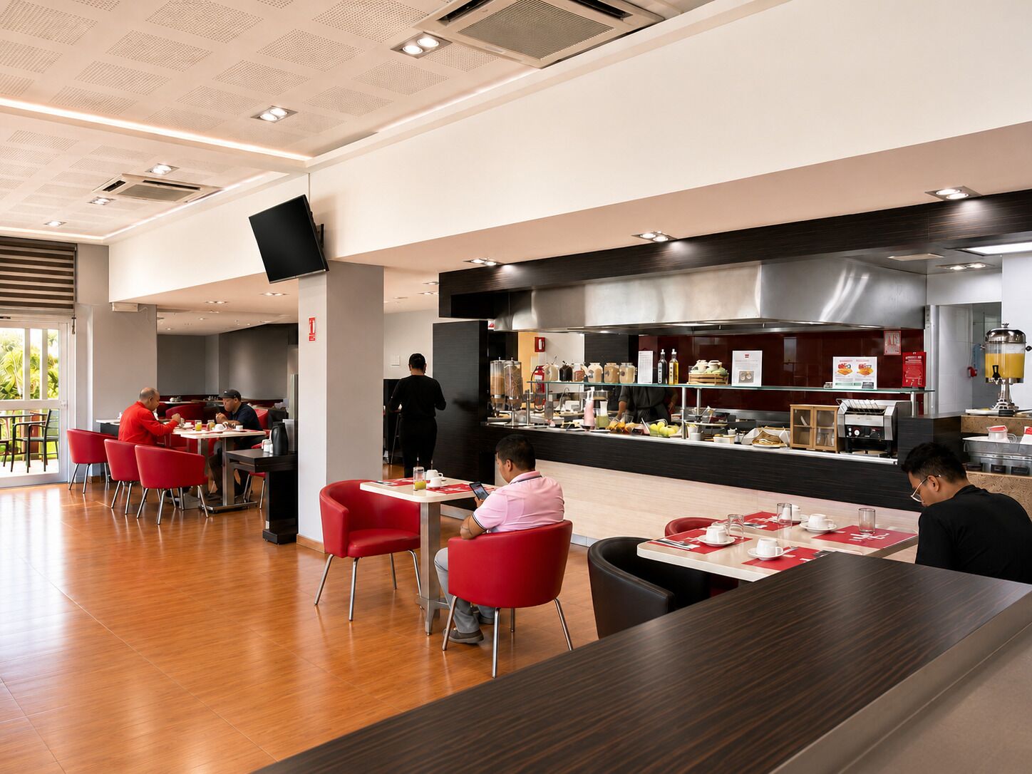 Un espace repas moderne avec des chaises rouges, un long comptoir et une cuisine en arrière-plan.