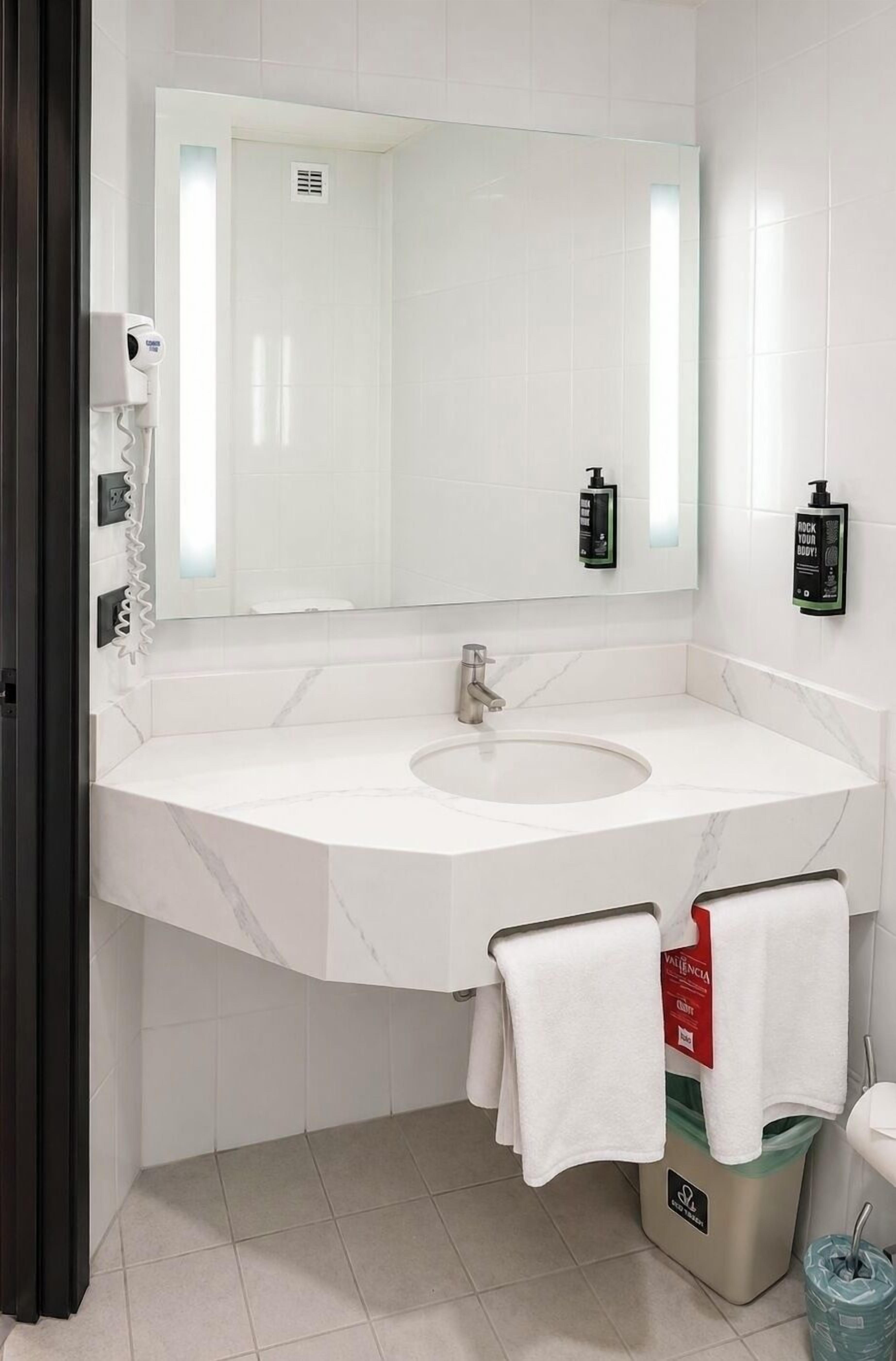 A bathroom with a white marble sink, a large mirror, a towel rack, and a trash bin.