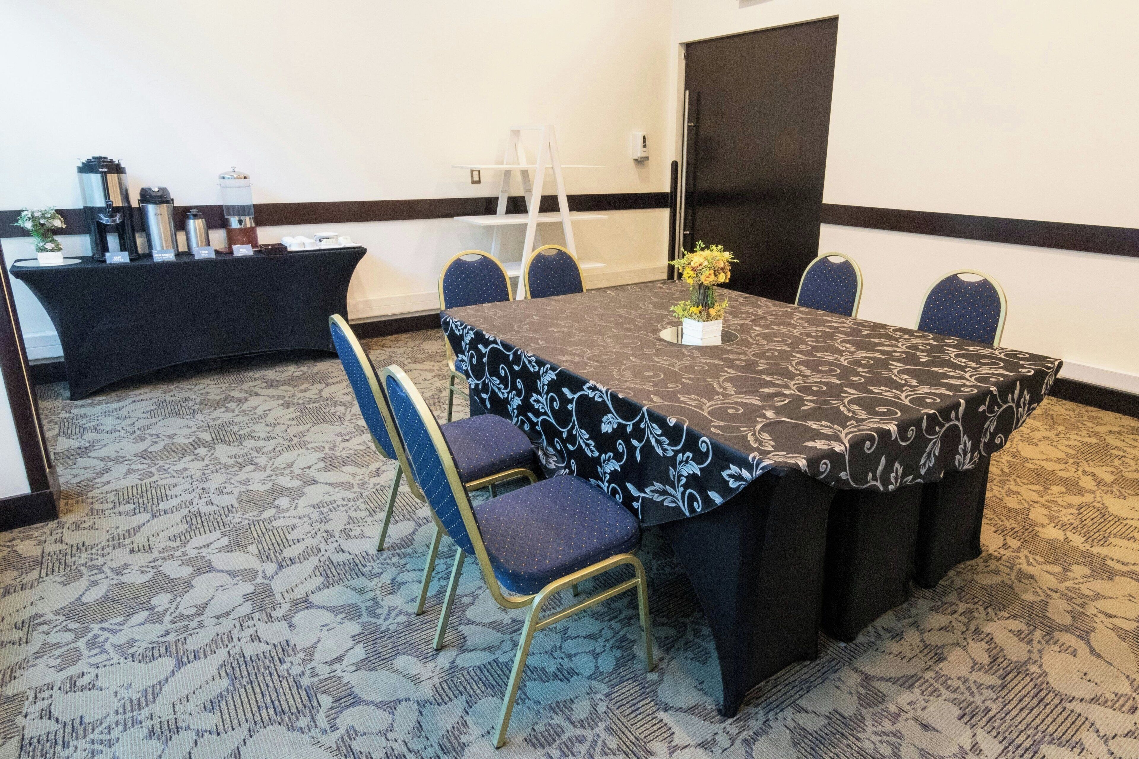 A conference room with a large table, six chairs, a coffee station, and a flower vase.