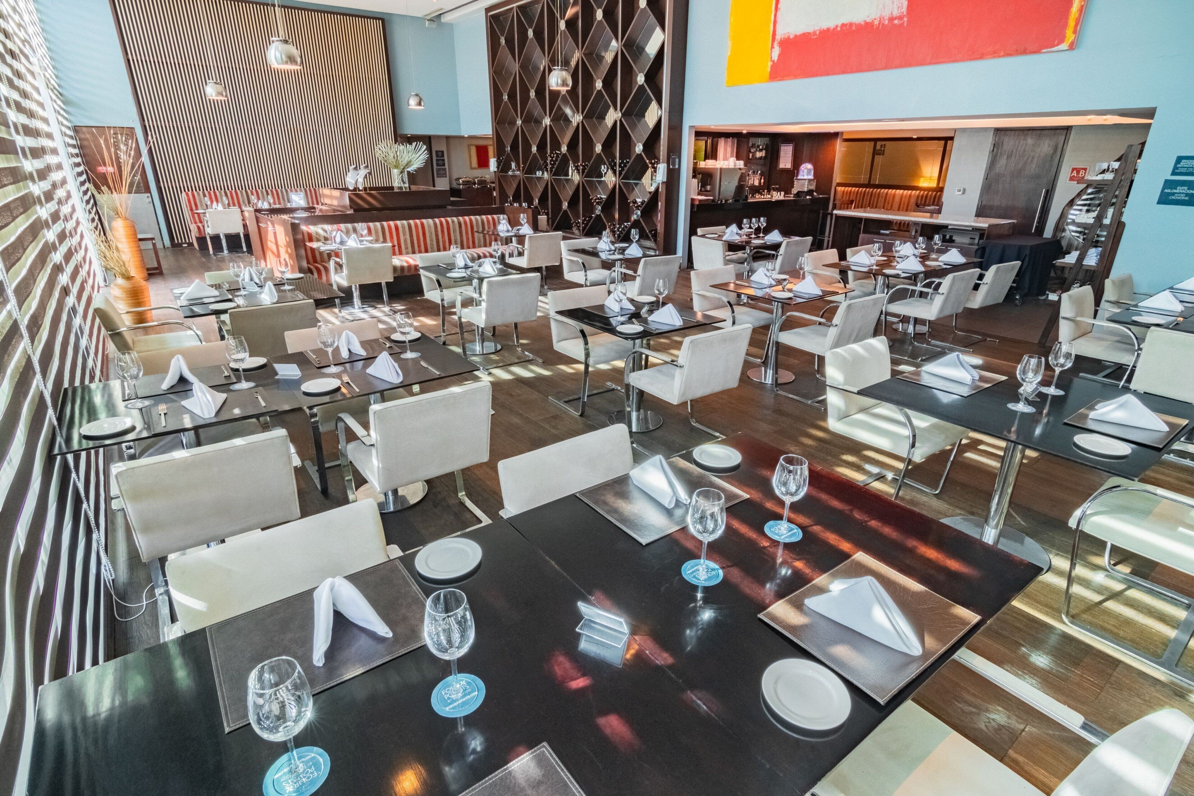 A modern restaurant with multiple dining tables, each set with white napkins, plates, and wine glasses.