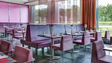 Un restaurante con asientos y mesas moradas, ventanas amplias y vistas al exterior con vegetación.