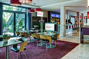 A modern hotel lobby with a bar area, seating arrangements, and a large screen displaying the hotel name. - IntercityHotel Berlin Airport Area North (Schoenefeld)
