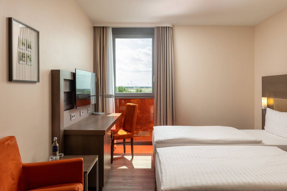 A hotel room with a bed, a desk, a chair, a TV, and a window with curtains.