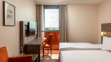 A hotel room with a bed, a desk, a chair, a television, and a window with curtains.
