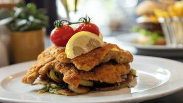 Une assiette de nourriture panée et frite, probablement du poulet, garnie d’une tranche de citron et de tomates cerises.