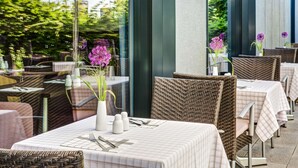 Un área de comedor al aire libre con sillas y mesas de mimbre, algunas con sombrillas.