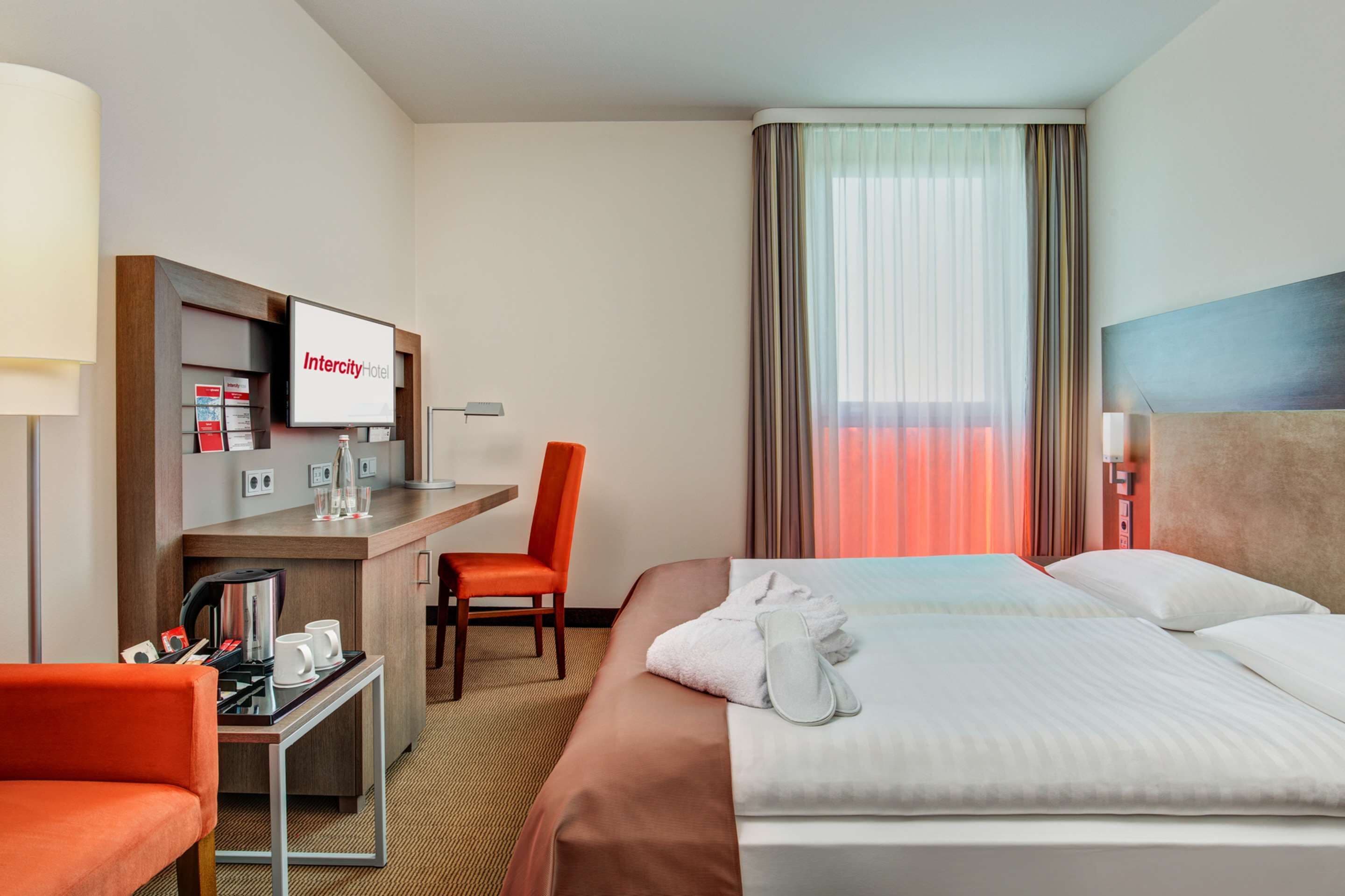 Una habitación de hotel con cama, escritorio, silla, televisor y ventana con cortinas.