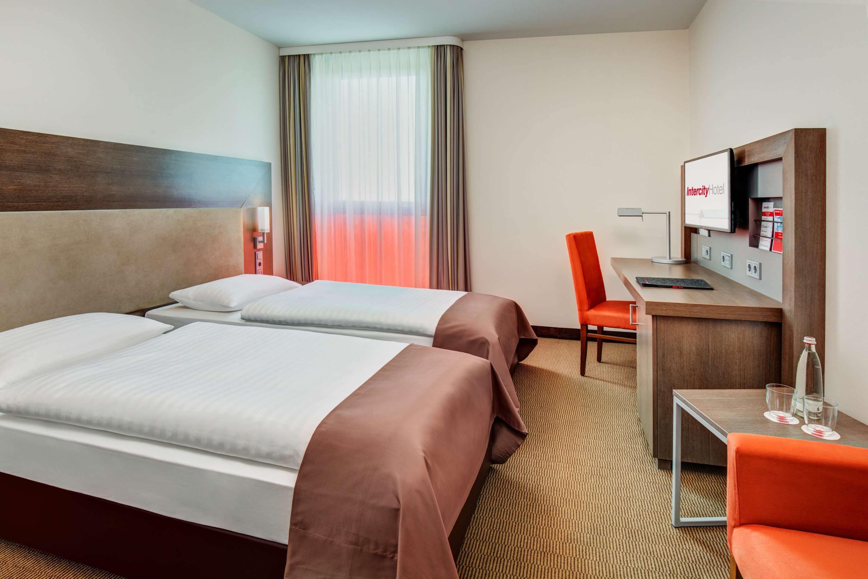 Habitación de hotel con dos camas, un escritorio, una silla, un televisor y una ventana con cortinas.