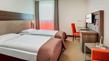 Habitación de hotel con dos camas, un escritorio, una silla, un televisor y una ventana con cortinas.