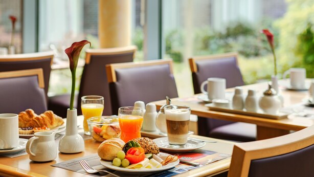 Desayuno con croissants, fruta, jugo y café sobre una mesa con vistas a la naturaleza.