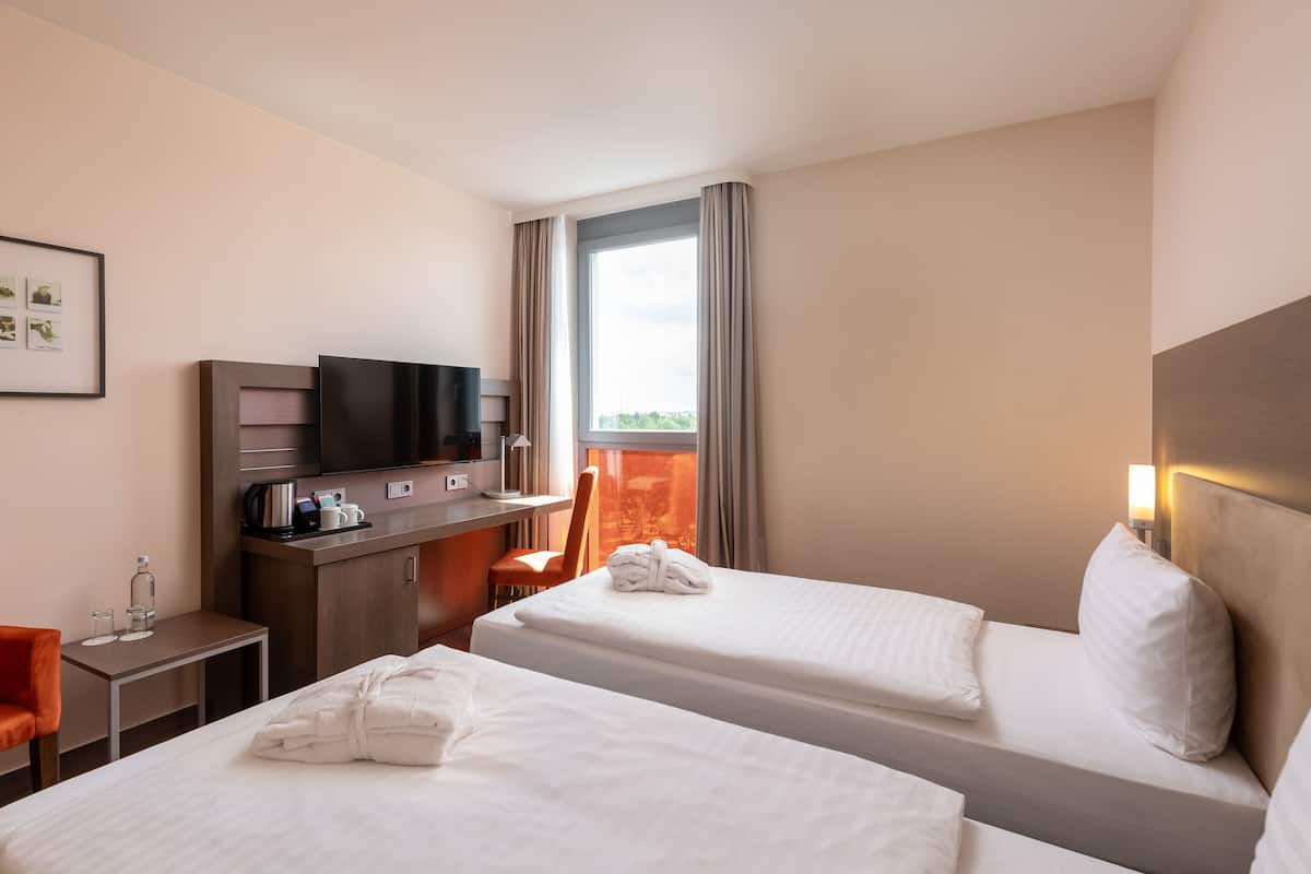 A hotel room with two beds, a desk with a TV, a chair, and a window with curtains.