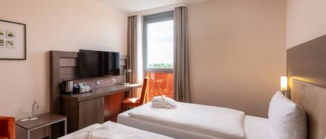 Quarto de hotel com duas camas, uma escrivaninha com televisão, uma cadeira e uma janela com cortinas.