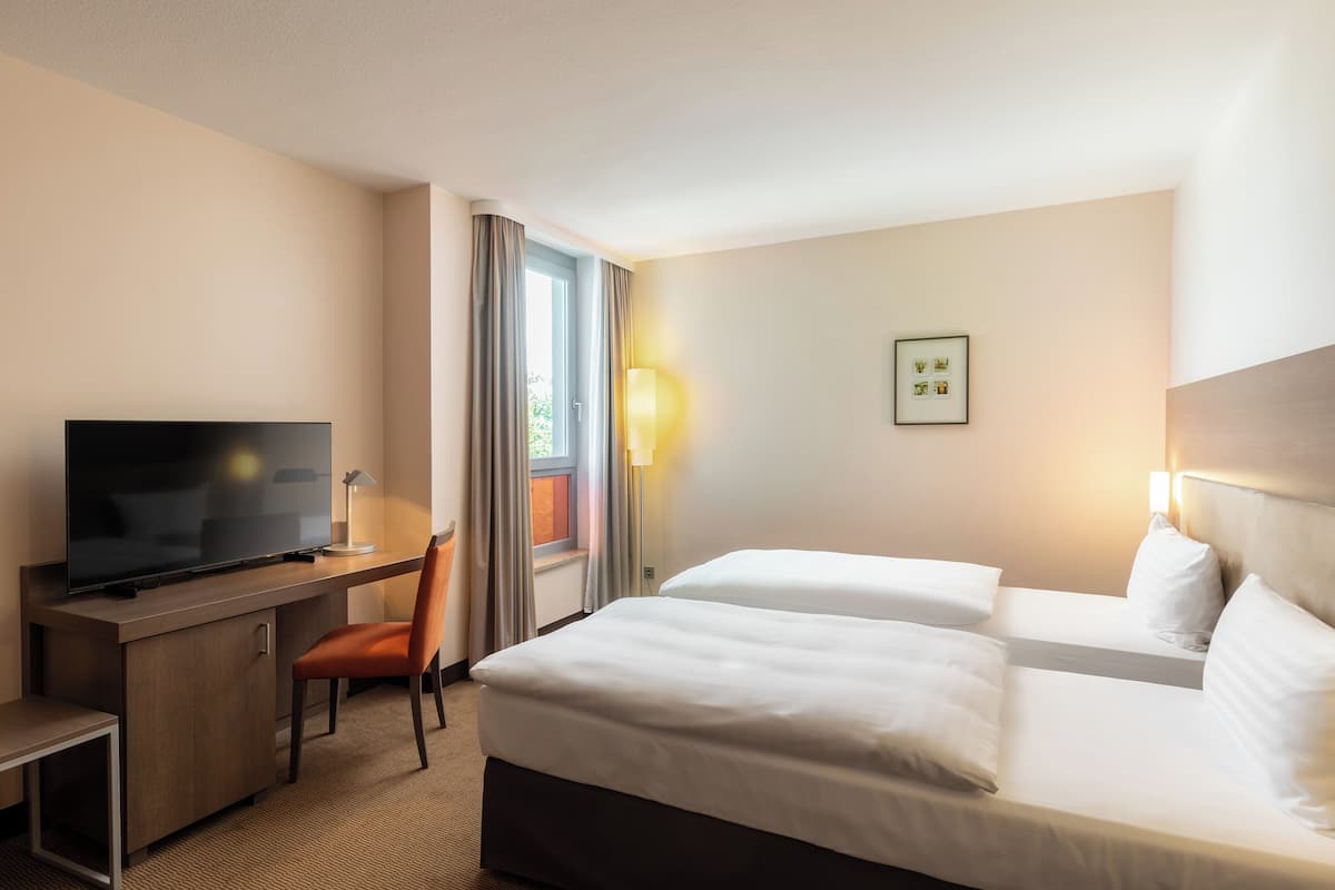 A hotel room with a flat-screen TV, a desk, two beds, and a window with curtains.