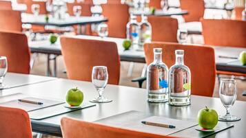 A dining area with orange chairs, tables set with wine glasses, apples, and a bottle of water.