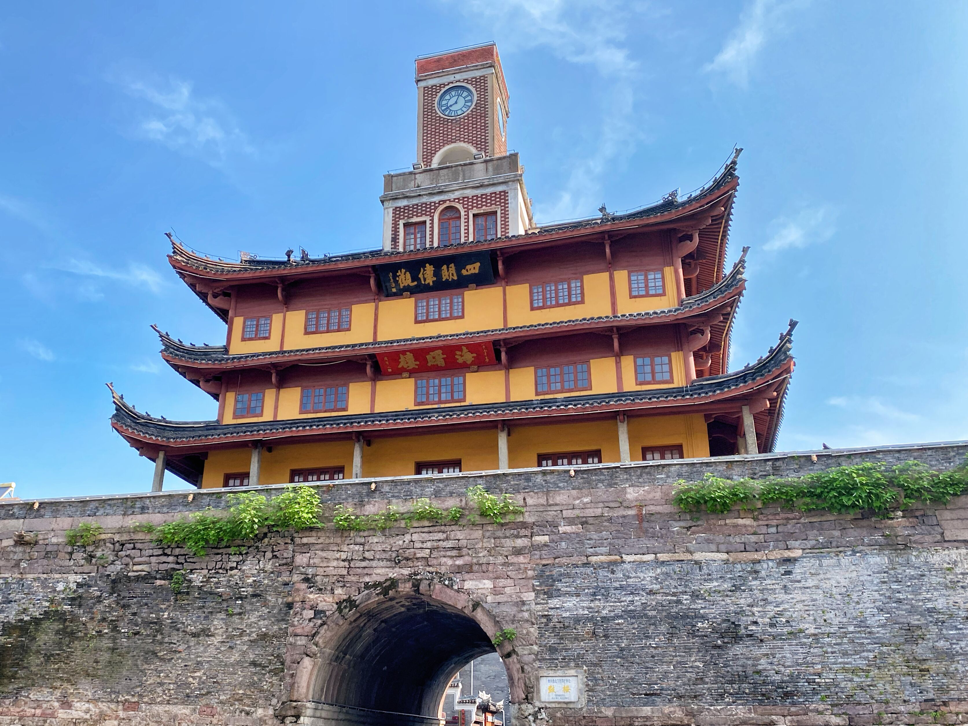 A traditional multi-story building with a clock tower, featuring a prominent entrance and a stone bridge with an archway.
