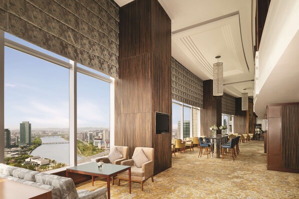 A spacious hotel lobby with large windows offering a city view, a seating area with sofas and chairs, and a dining space with tables and chairs. - Shangri-La Ningbo (Ningbo)