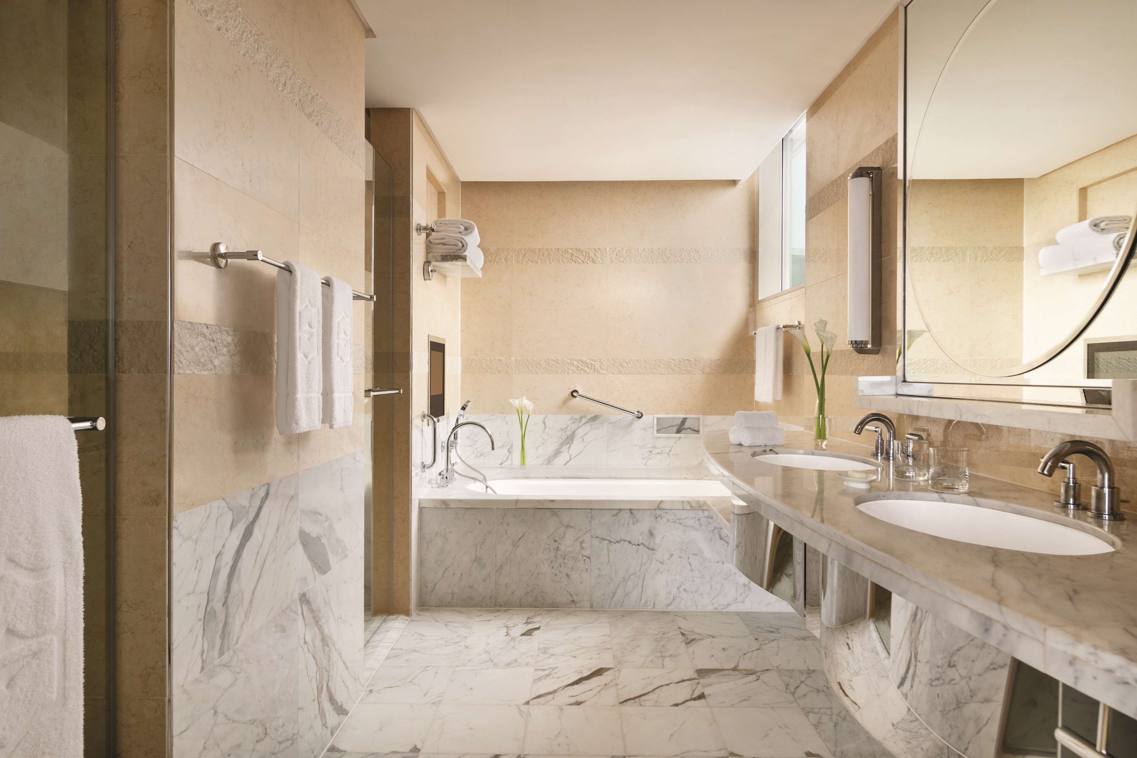 A modern bathroom with a large bathtub, two sinks, and a glass shower enclosure.