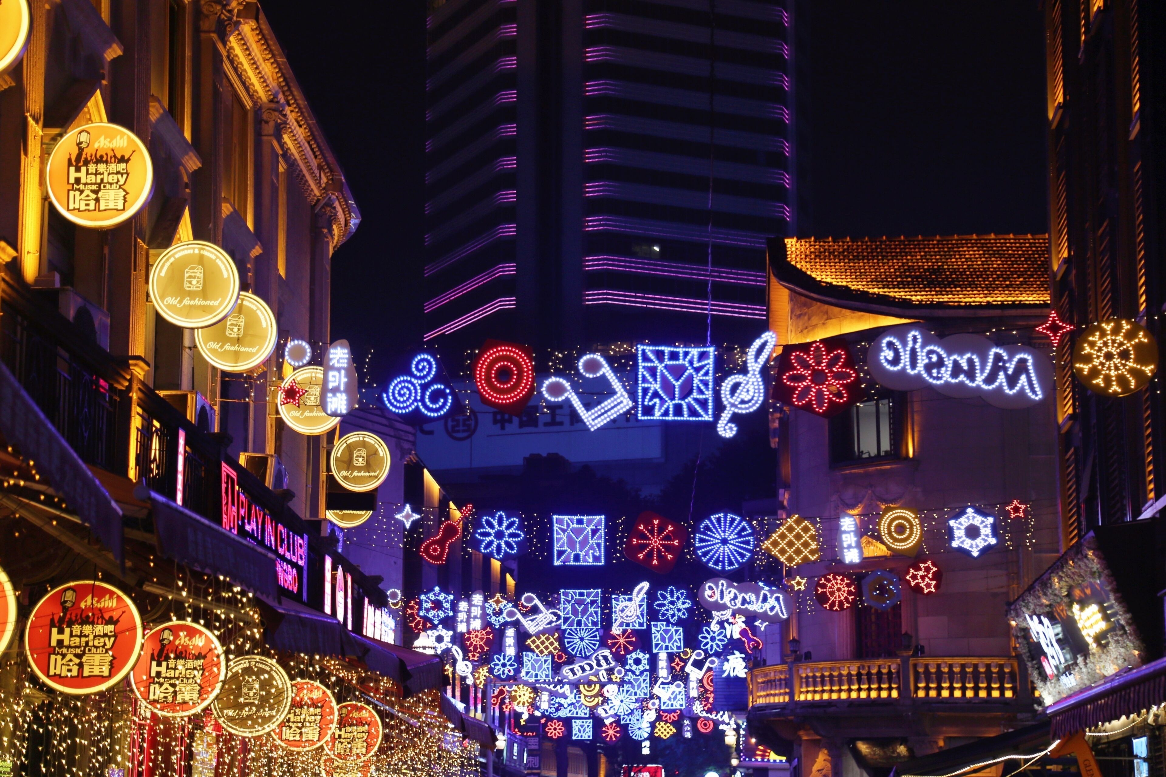 A brightly lit street with various illuminated signs and decorations, including circular and star-shaped lights.