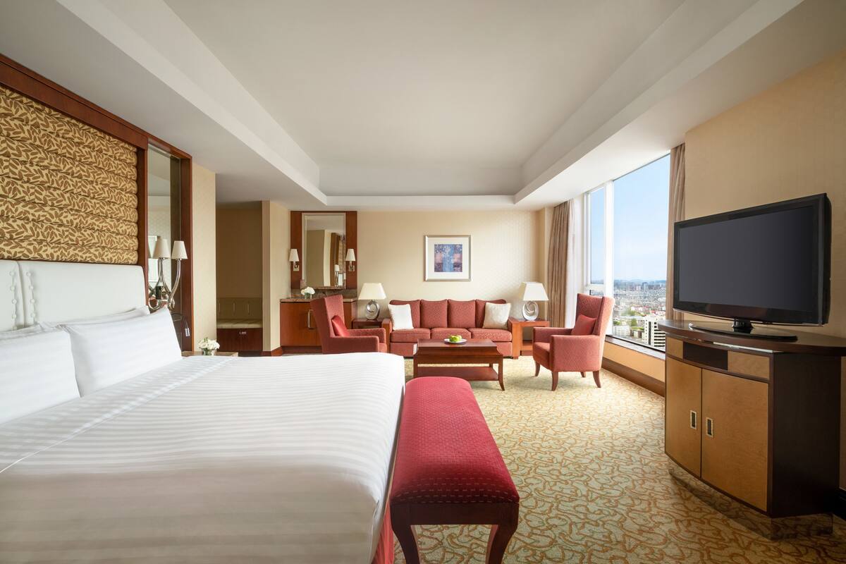 Habitación de hotel con una cama grande, un sofá, un televisor y vistas a la ciudad.