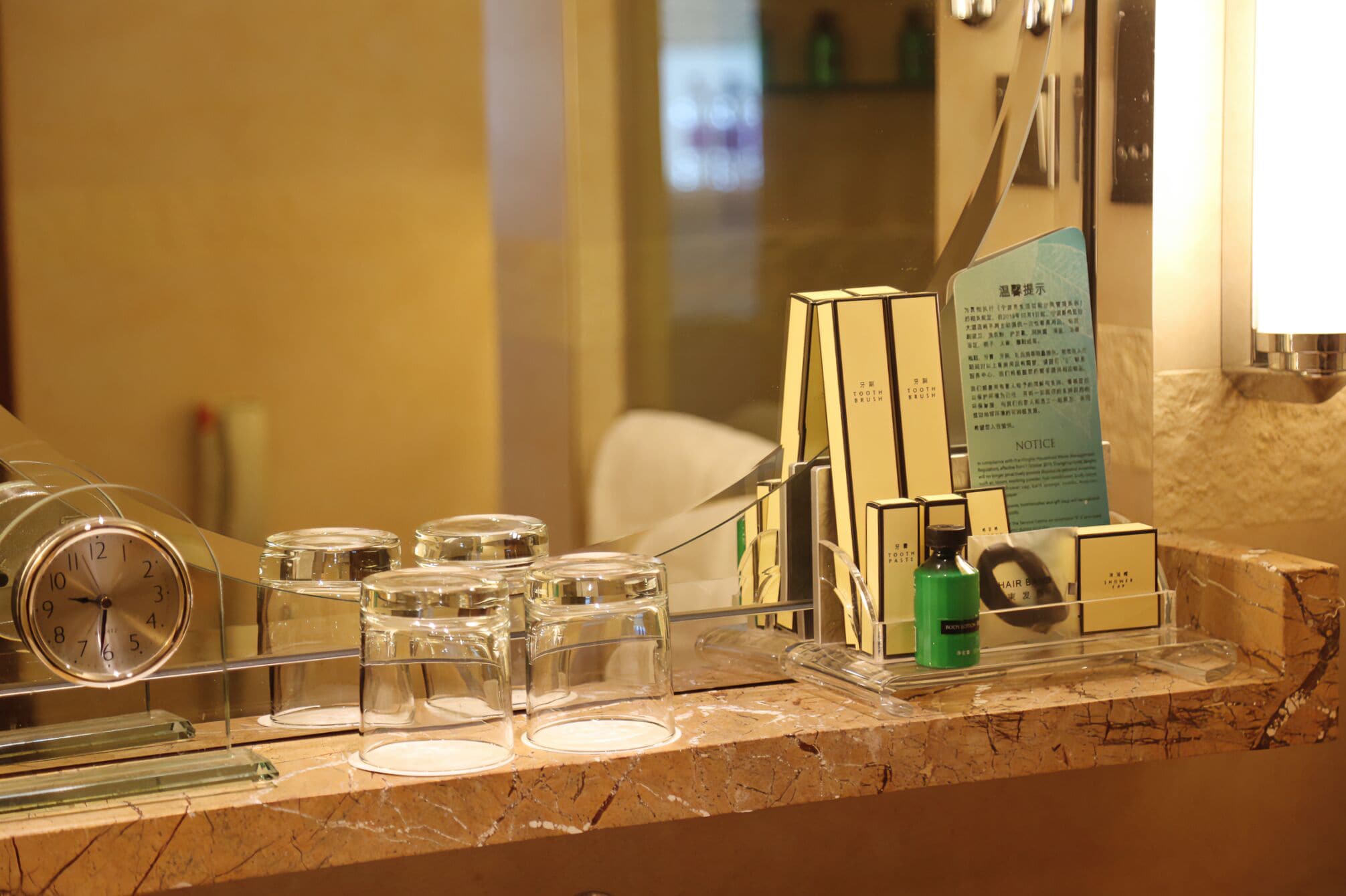 Un'area della reception di un hotel con un bancone in marmo, una sveglia e diversi articoli da toilette e per la cura personale esposti in contenitori trasparenti.