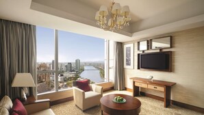 Habitación de hotel moderna con un gran ventanal que ofrece vistas a la ciudad, un sofá cómodo, una mesita redonda pequeña y un televisor de pantalla plana montado en la pared.
