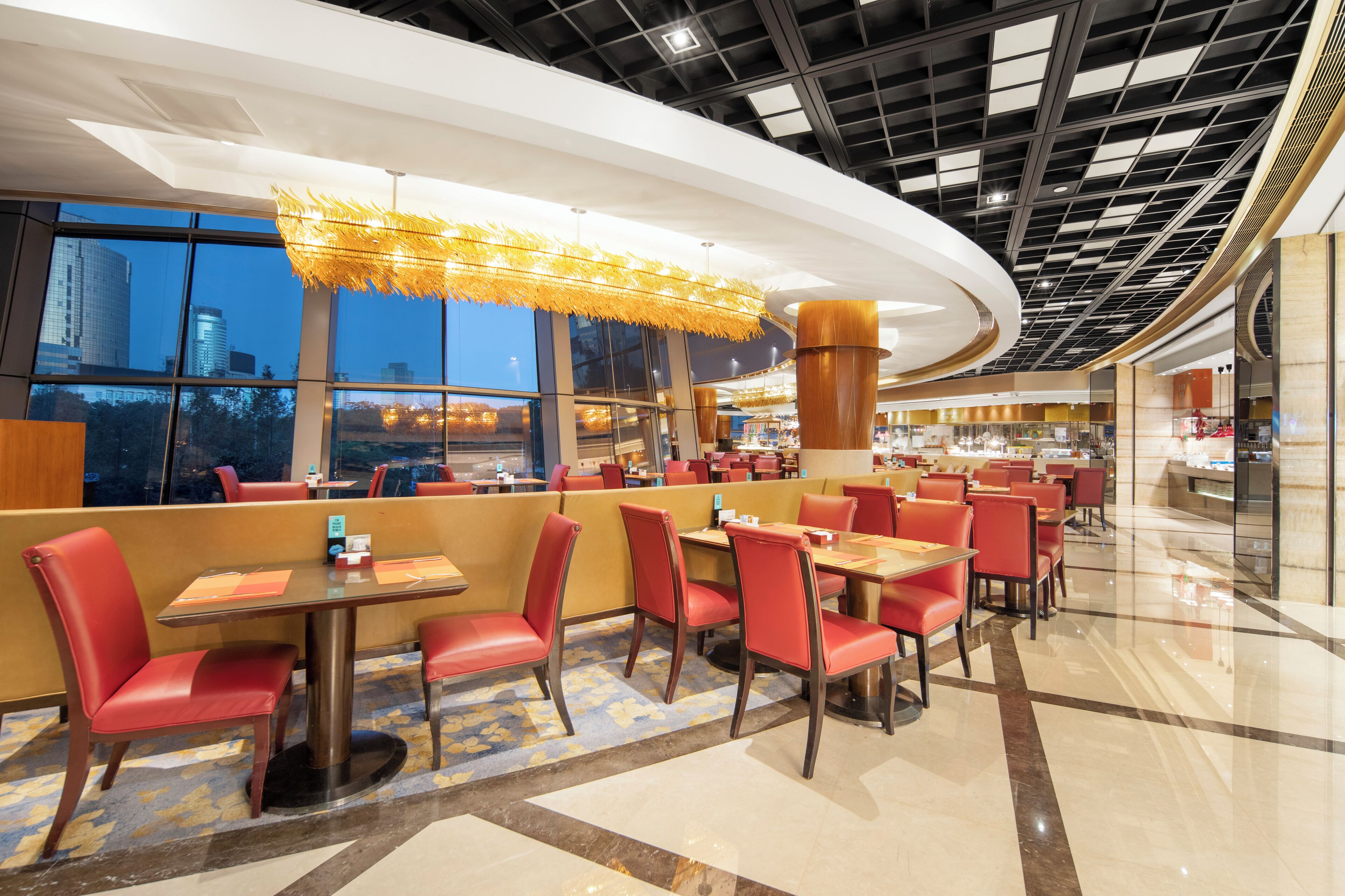 Un restaurante moderno con sillas y mesas rojas, ventanas amplias y un techo con diseño de cuadrícula.