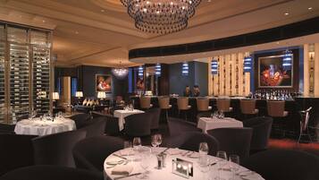 A restaurant with round tables set for dining, a bar area with bottles, and a large chandelier.