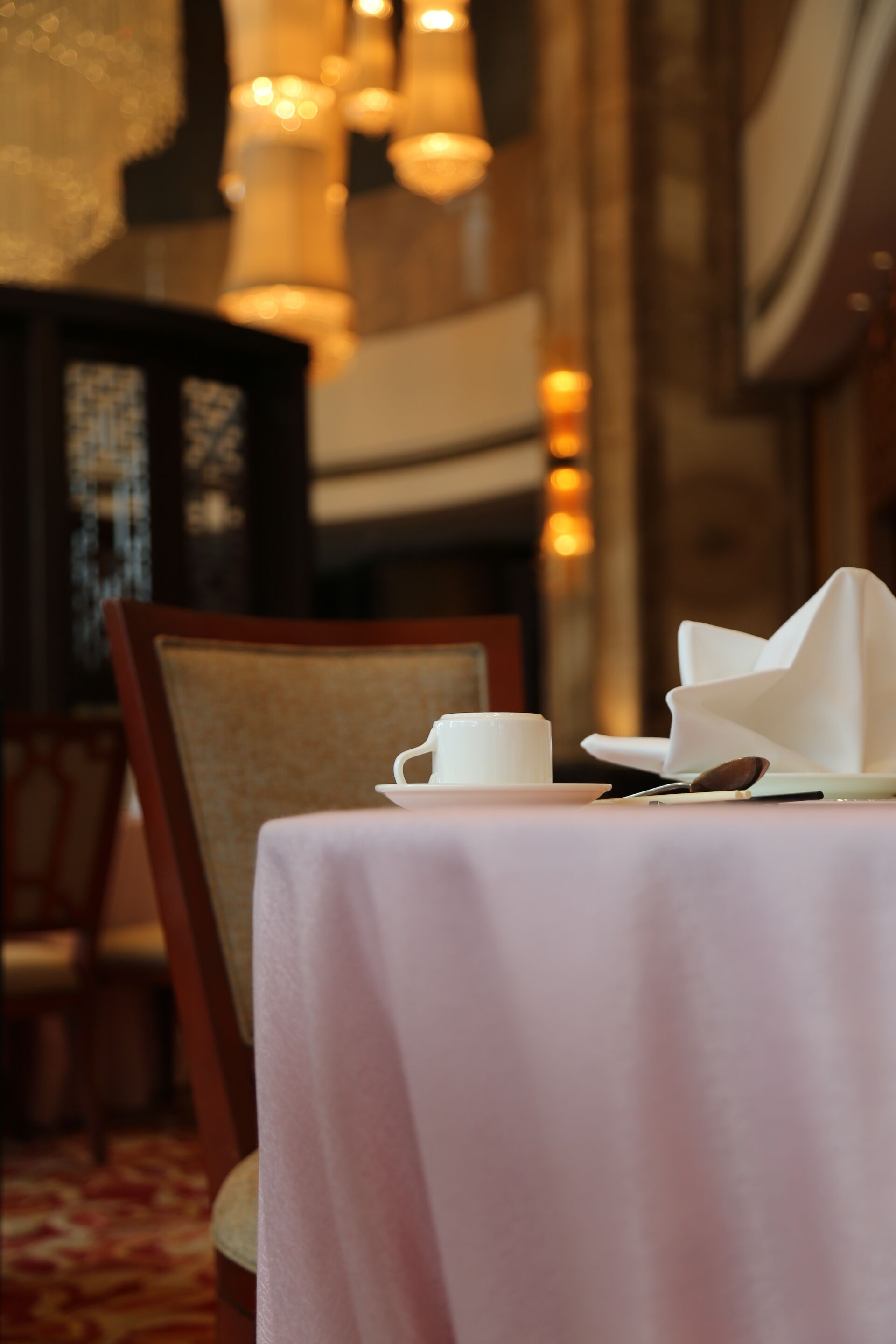 A dining table with a white tablecloth, a cup, a spoon, and a napkin.