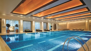 Una piscina interior moderna con suelo de mosaico azul, paneles de techo de madera y zonas de descanso a lo largo de las paredes.