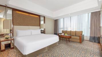 A hotel room with a large bed, a sofa, a small table with fruit, and a mirror.