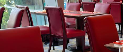 A restaurant interior with red chairs and tables, a glass coffee cup, and plates with food.