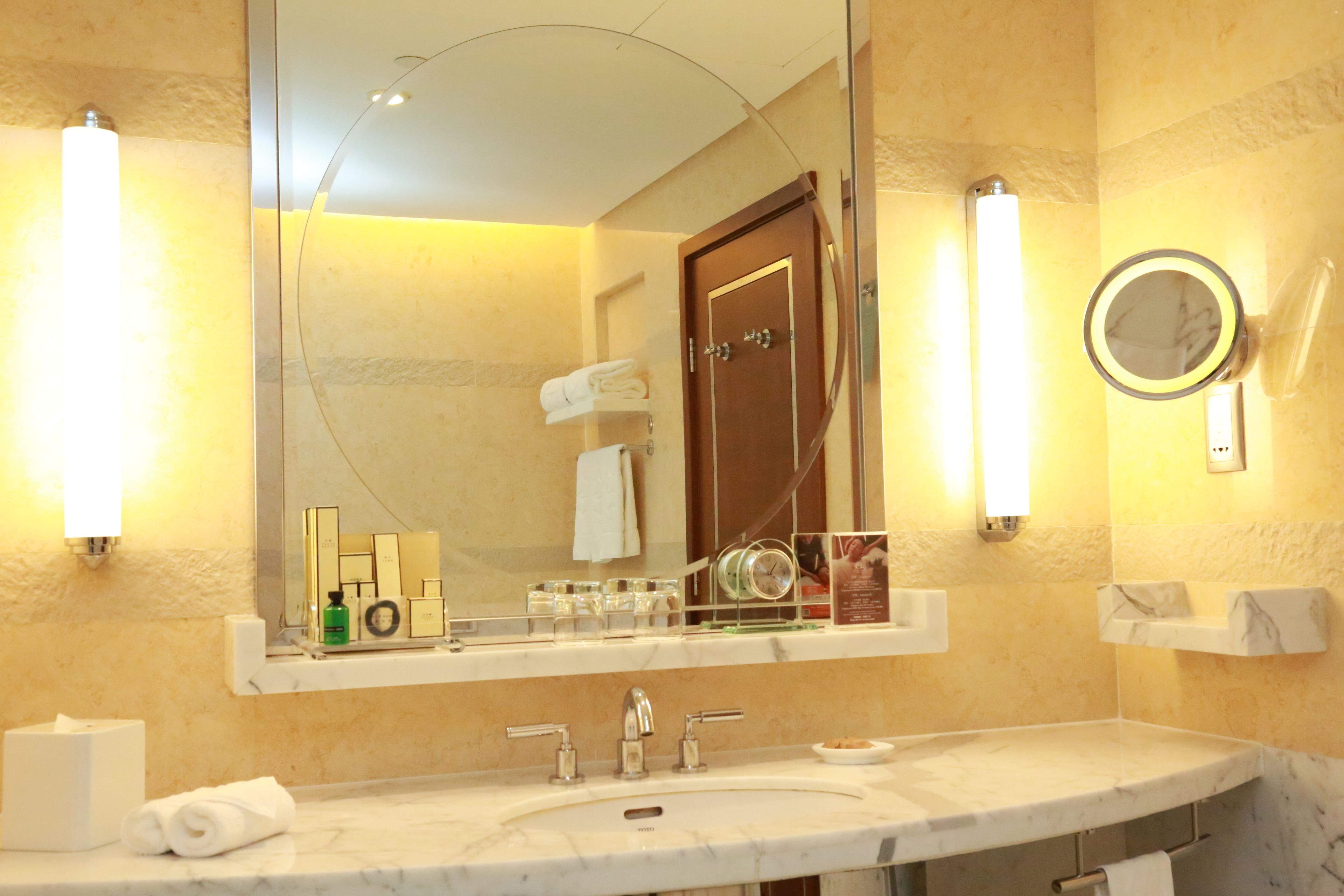 Une salle de bain avec un lavabo en marbre, un grand miroir et deux appliques murales.