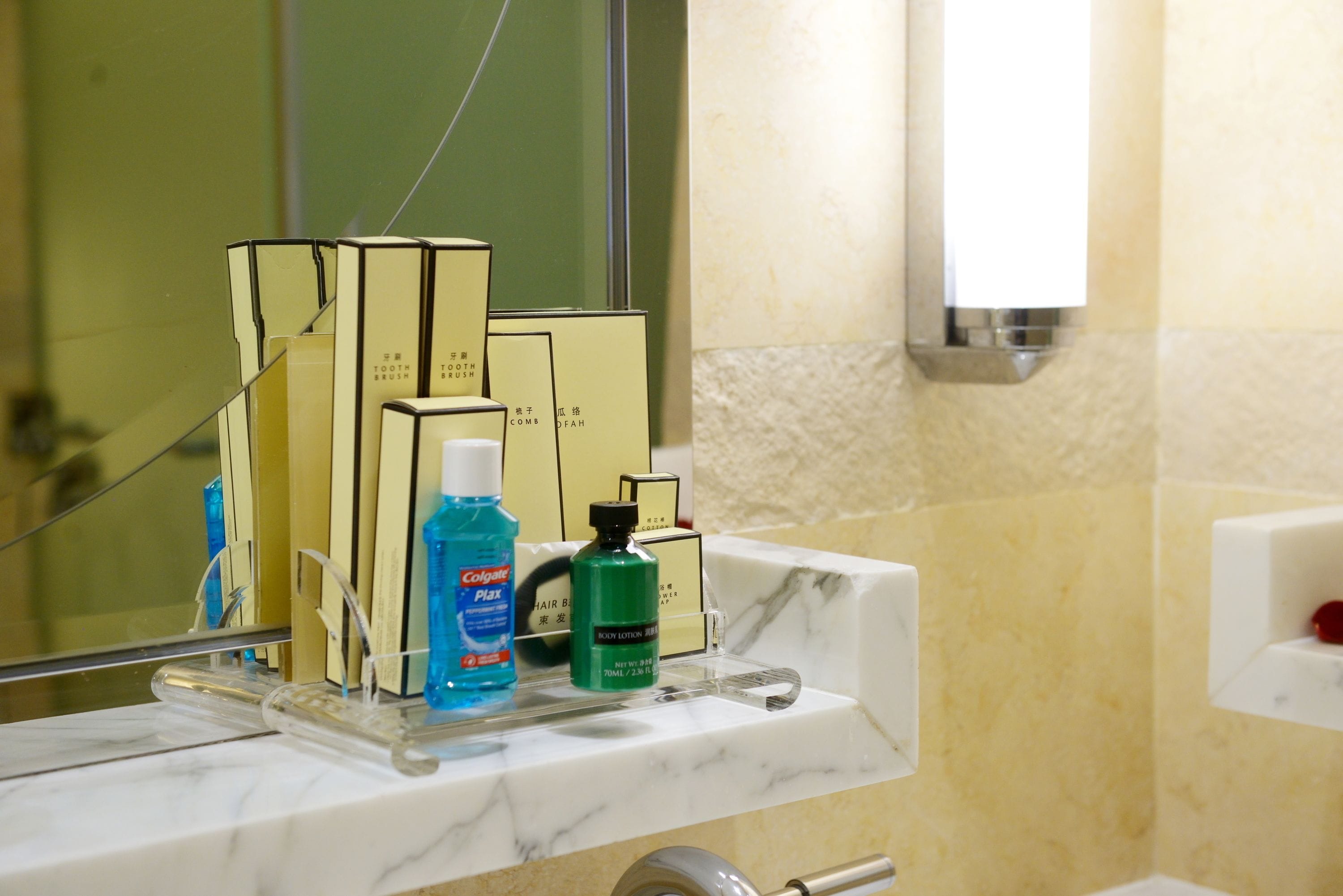 Ein Badezimmer mit Marmorplatte, einem Spiegel und verschiedenen Pflegeprodukten, darunter eine Zahnbürste, Zahnpasta und eine Flasche Körperlotion.
