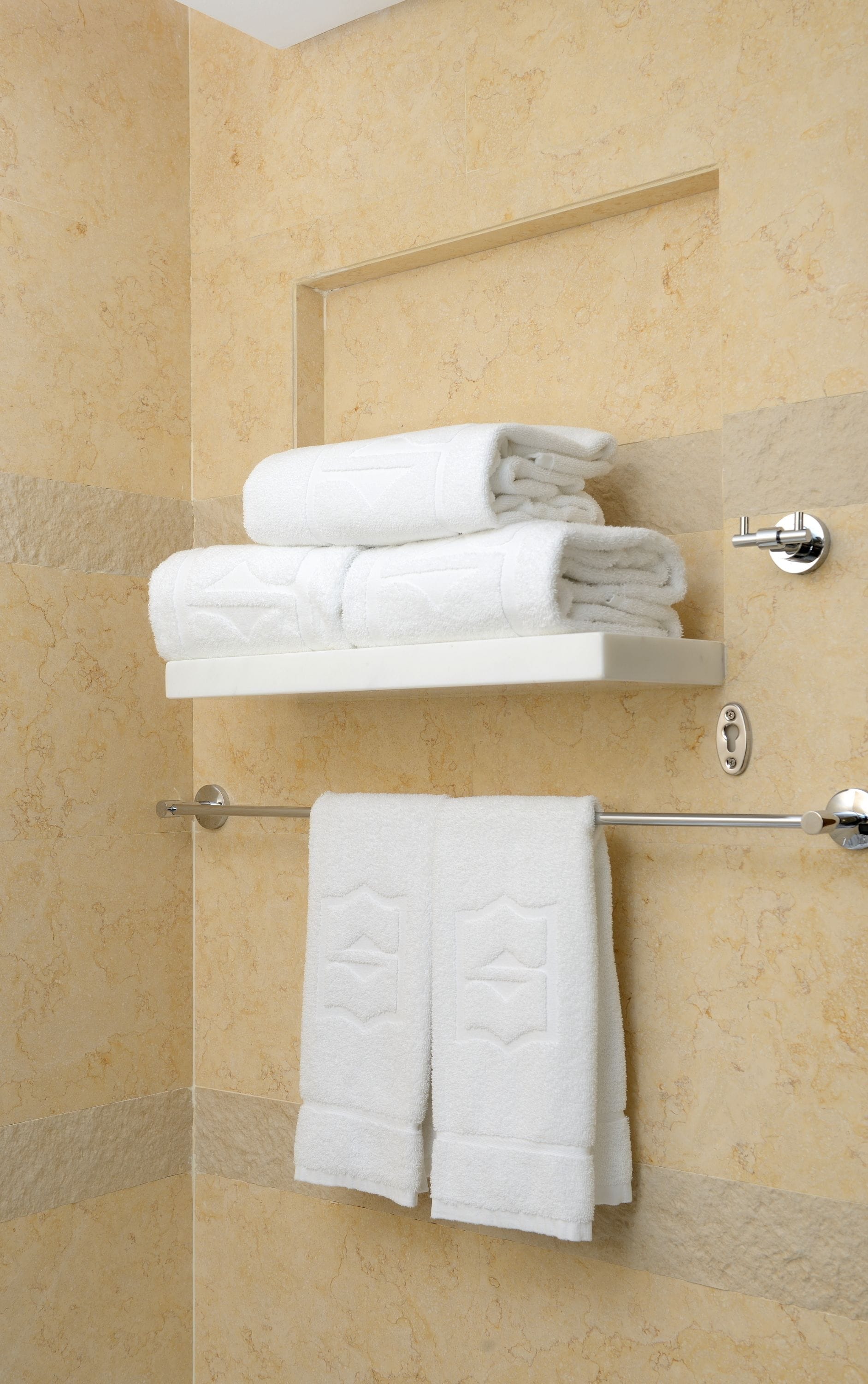 A bathroom with beige marble walls, a white towel rack, and a towel shelf.