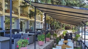 An outdoor seating area with wicker furniture, potted plants, and a covered section with tables and chairs. - Shipka (Golden Sands)