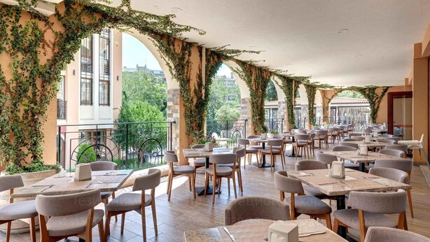 A restaurant with outdoor seating, covered by arches with greenery, and a view of buildings and trees. - Festa Via Pontica (Pomorie)