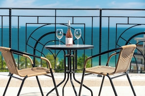 A table with two chairs and a bottle of wine, set against a railing with a view of the sea.