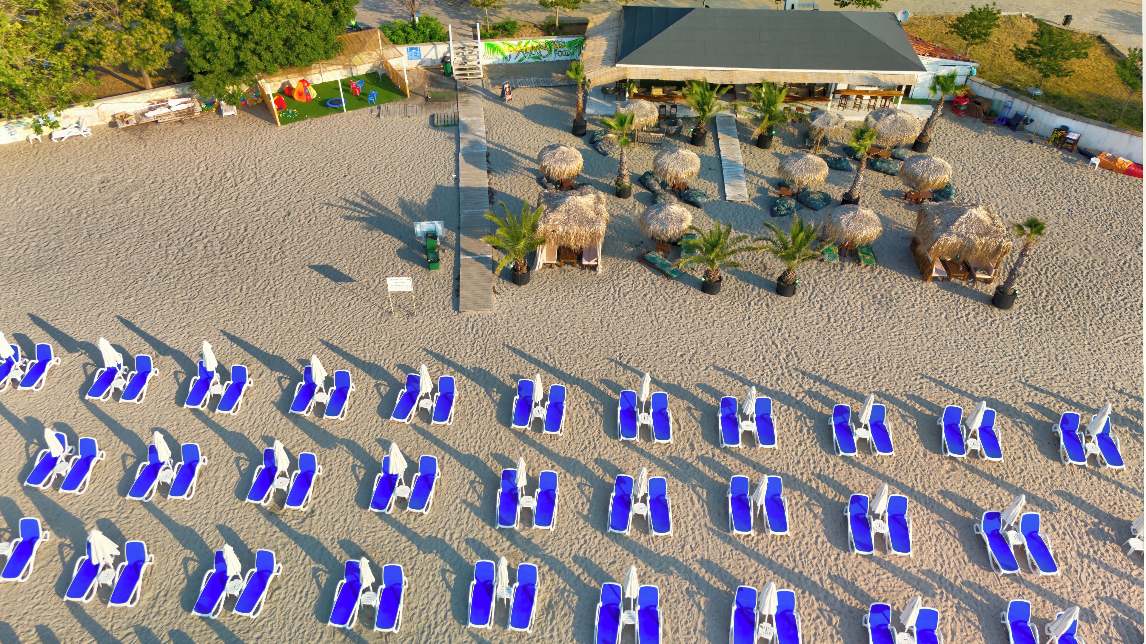 Une plage bordée de rangées de chaises longues bleues et d’ombrelles en chaume.