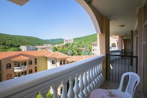 A balcony with a white balustrade overlooking a town with red-roofed buildings and green hills.