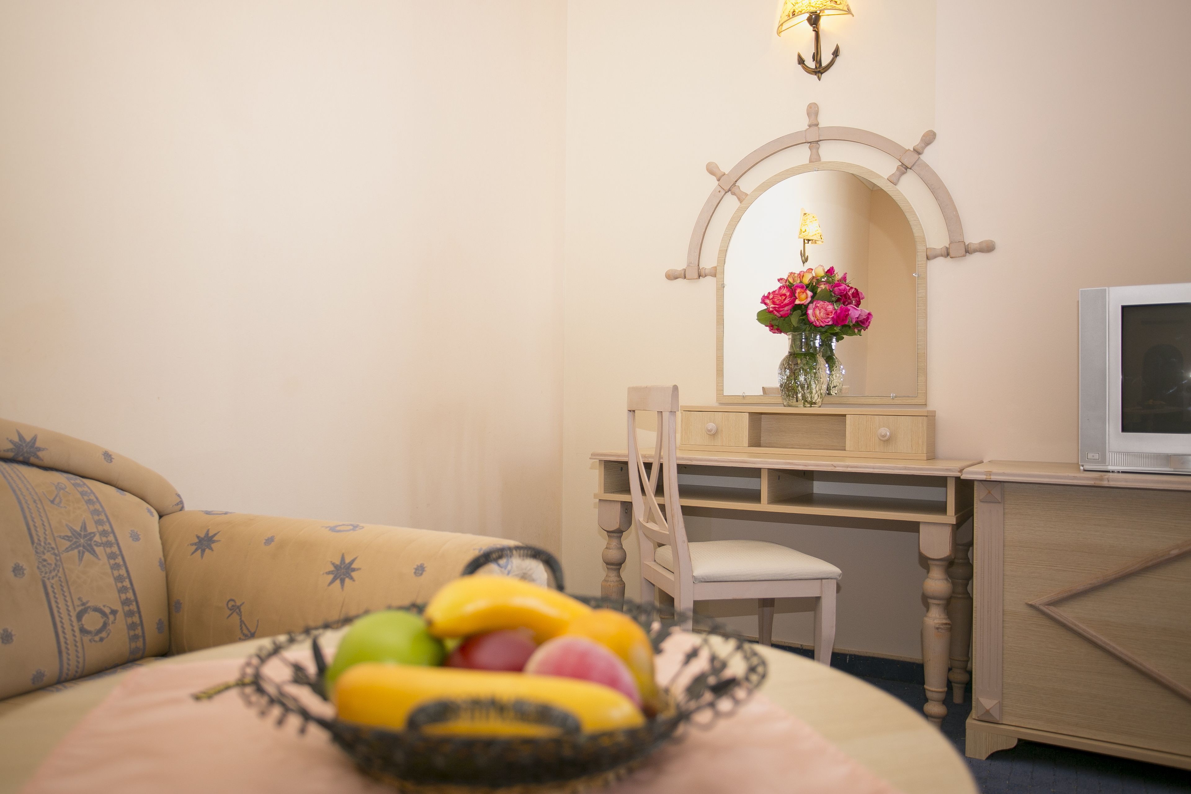 Habitación de hotel con cama, escritorio, silla, televisor y espejo con un florero.