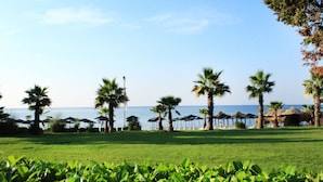 A grassy area with palm trees and beach umbrellas, suggesting a resort setting. - Royal Park Hotel - All Inclusive (Elenite)