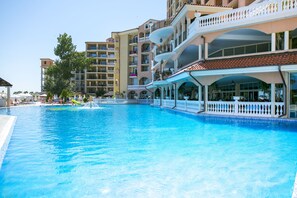 A large swimming pool with a white fence and a multi-story building with balconies in the background.