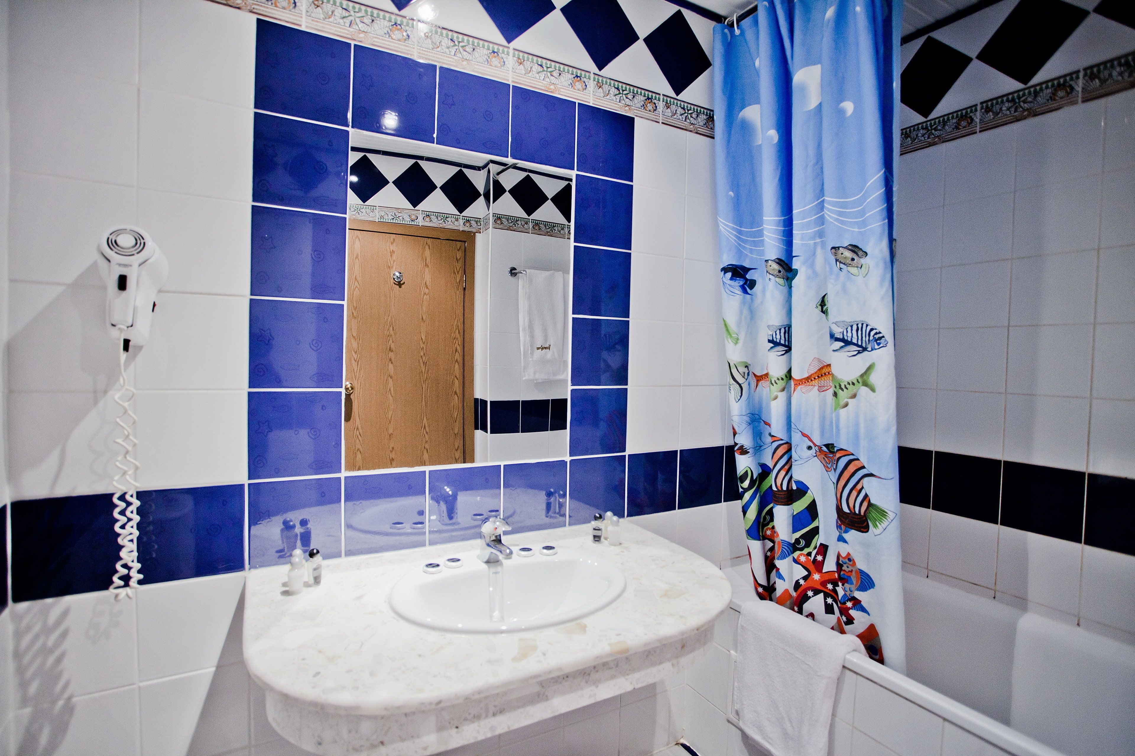 A bathroom with a white sink, a mirror, and a shower curtain with fish designs.