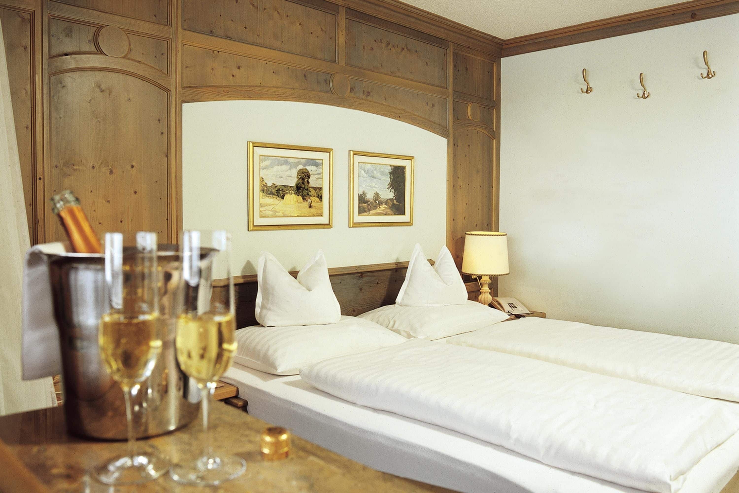 A hotel room with a wooden headboard, two framed pictures on the wall, a bedside table with a lamp, and a bed with white bedding.