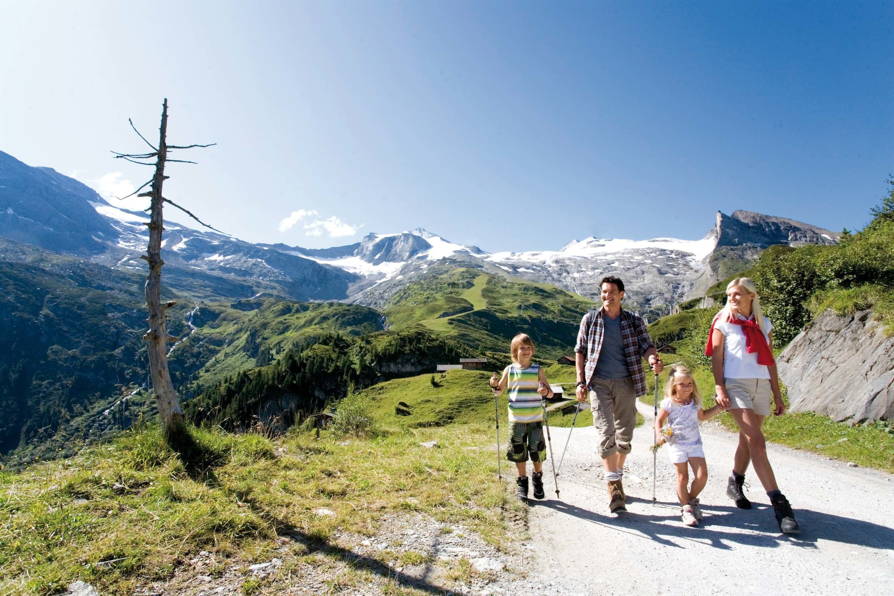 Una familia caminando por un camino de montaña con montañas nevadas al fondo.