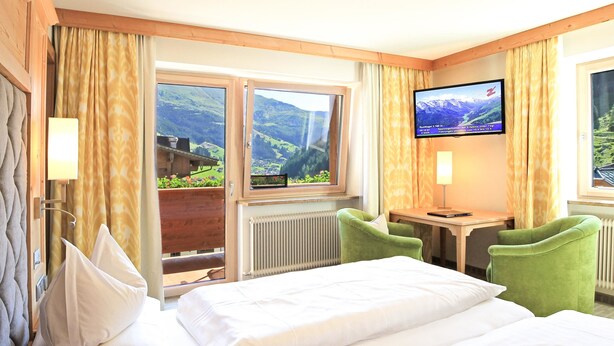 Habitación de hotel con cama, escritorio, televisor y vistas a las montañas.